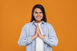 Thank you gesture. Beautiful grateful woman with hands clasped together on orange background