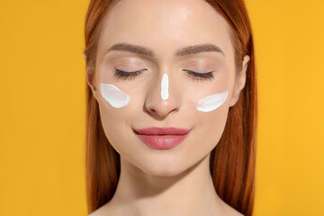 Poster - Beautiful young woman with sun protection cream on her face against orange background, closeup