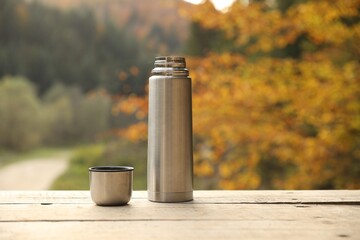 Sticker - Metallic thermos and cup lid on wooden table outdoors, space for text