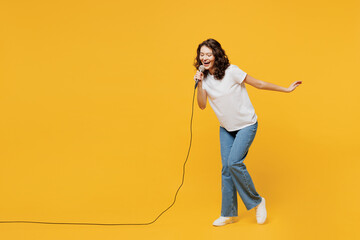 Wall Mural - Full body singer happy fun young woman wear white blank t-shirt casual clothes sing song in microphone at karaoke club isolated on plain yellow orange background studio portrait. Lifestyle concept.