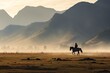 Landscape photography capturing a peaceful scene of a rider and horse against a mountain backdrop, enveloped in early morning mist, evoking tranquility.