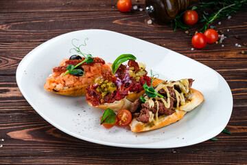 Wall Mural - Bruschetta with beef, salmon, sausage, sun-dried tomatoes, cream cheese, olives, pickles and sauce on wooden table.