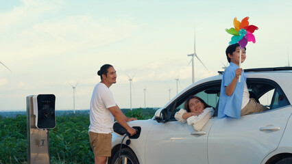 Sticker - Concept of progressive happy family enjoying their time at wind farm with electric vehicle. Electric vehicle driven by clean renewable energy from wind turbine generator for charging station.