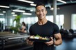 Male sports nutritionist holding a healthy meal box in a gym setting.