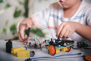 Little child remotely learn online with car toy before sent code, Asian kid boy plugging energy and signal cable to sensor chip with Arduino robot car, STEAM education AI technology course learning