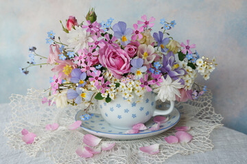 Wall Mural - Bouquet of spring and summer flowers in a cup on the table, roses, aquilegia, spirea, forget me not flowers, pansies, violet, beautiful postcard, still life, blur.