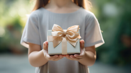 Sticker - A child holding a pink gift box tied with a satin ribbon bow, with a warm bokeh light background.