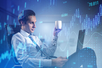 Poster - Attractive young businessman sitting and using laptop with glowing candlestick forex chart on blurry office interior background. Stock market and investment concept. Toned image. Double exposure.