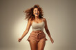 © Марина Демешко - A young happy smiling red-haired woman in short shorts and crop top with her eyes closed dancing on a monochrome light background. Plus size model, overweight girl. Body positive