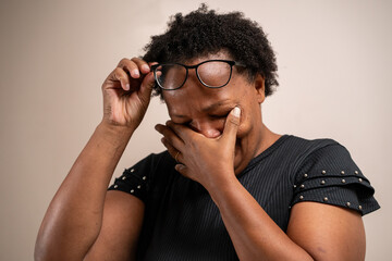 Black woman with hand on eyes crying on pastel background.