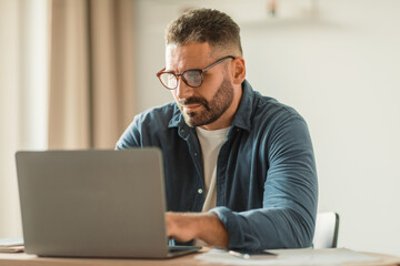 Poster - Serious middle aged man types focused on his laptop indoor
