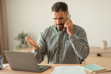 Poster - stressed man talking on cellphone managing tasks on laptop indoor