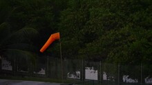 An Orange Windsock Gracefully Flutters In The Tropical Breeze Against The Backdrop Of A Vibrant And Lush Forest, Capturing The Essence Of Nature's Motion. 