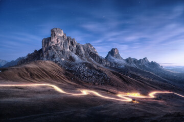 Wall Mural - car light trails on mountain road and high rocks at night in autumn in passo giau, dolomites, italy.