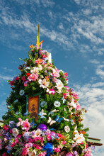 A Tall Lush Green Christmas Tree Decorated With Colorful Bright Exotic Flowers. The Vivid Blooms Are Orange, Yellow, Pink, And Red Color Orchids. The Zero Waste Decorations Are On A Tree Outdoors. 