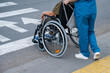 © Михаил Решетников - Rear view of a nurse helping an elderly woman in a wheelchair cross the road.