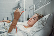 © Daniel - Gadget addiction. Calm smiling young woman or teenage girl lying at cozy bed holding cellphone in hands looking at screen chatting checking social network account before fall asleep or after waking up