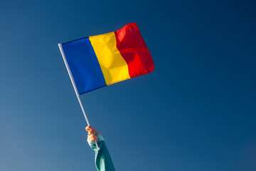 Wall Mural - Hand Waiving a Romanian Flag on a Blue Sky. Cheerful enthusiastic patriotic person displaying the symbol of Romania
