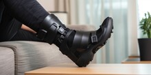 Ankle Sprain Orthosis, Black Splint, Walker Boot On Leg Sitting On The Sofa At Home. Ankle Foot Orthosis Close-up, Generative AI