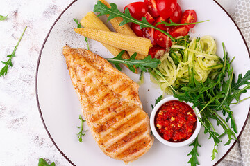 Healthy keto, ketogenic lunch with grilled chicken  breast, fillet and  salad of arugula, onion, boiled corn, cucumber and tomato. Roasted chicken meat and salad. Top view, flat lay