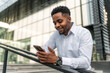 © DusanJelicic - A portrait of a handsome Black businessman leaning against a railing during his break, holding a phone in his hand.