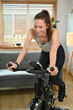 © Prathankarnpap - Beautiful caucasian woman in sportswear training on smart stationary bike at home