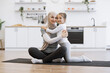 © sofiko14 - Adorable girl in sport outfit standing on knees on mat while trading positive energy with mom during exercises. Loving muslim female in hijab hugging daughter during fitness routine at home.
