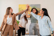 © Studio Marmellata - Happy young women colleagues standing and giving high five to each other while celebrating success in modern creative office during business meeting