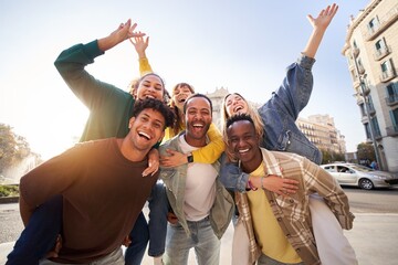 Portrait excited multi-ethnic group happy young friends piggyback enjoying great time outdoors and having fun together. Cheerful men carrying girlfriends on back. Looking at camera on vacation