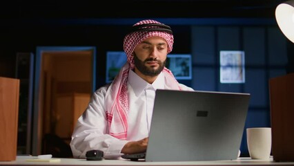 Poster - Arab employee concentrating on finishing up important job tasks, remotely working from stylish apartment personal office. Focused muslim teleworker typing on laptop keyboard