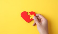 Hand Hold Two Pieces Red Heart Jigsaw Puzzle On Yellow Background. Health Care Love Wellbeing Organ Donation Family Insurance Concept. World Health Day Heart Day Theme.  Generative AI