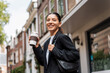 © Andrei - Stressless multiracial young businesswoman with a cheerful expression, in the street, holding a thermo cup of coffee