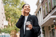 © Andrei - Stressless young businesswoman on the phone with a cheerful expression, in the street, holding a thermal cup of coffee