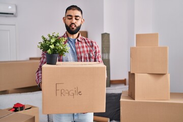 Wall Mural - Middle east man with beard moving to a new home holding cardboard box making fish face with mouth and squinting eyes, crazy and comical.