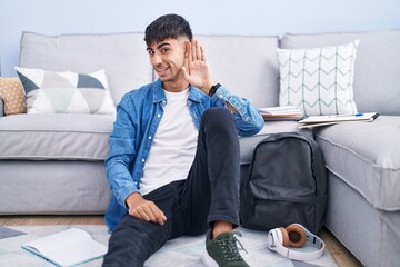 Sticker - Young hispanic man sitting on the floor studying for university smiling with hand over ear listening an hearing to rumor or gossip. deafness concept.