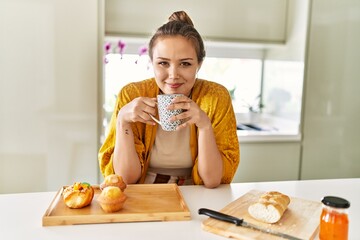 Poster - Young beautiful hispanic woman having breakfast drinking coffee at the kitchen