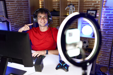 Sticker - Young hispanic man playing video games recording with smartphone smiling happy pointing with hand and finger