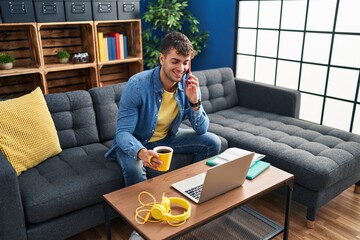 Poster - Young hispanic man student talking on smartphone drinking coffee at home