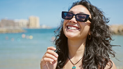 Wall Mural - Young beautiful hispanic woman tourist smiling confident wearing bikini and sunglasses at beach