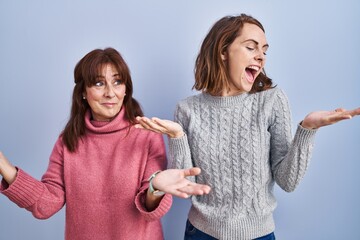 Poster - Mother and daughter standing over blue background smiling showing both hands open palms, presenting and advertising comparison and balance