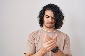 Poster - Hispanic man with curly hair standing over white background suffering pain on hands and fingers, arthritis inflammation