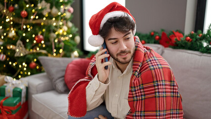 Wall Mural - Young hispanic man celebrating christmas talking on smartphone at home