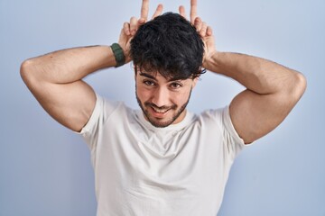 Canvas Print - Hispanic man with beard standing over white background posing funny and crazy with fingers on head as bunny ears, smiling cheerful