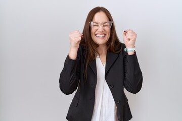 Wall Mural - Beautiful brunette woman wearing business jacket and glasses excited for success with arms raised and eyes closed celebrating victory smiling. winner concept.