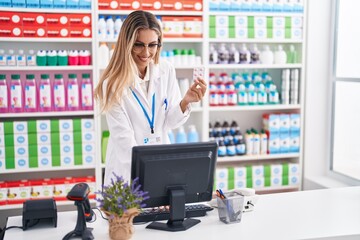 Poster - Young blonde woman pharmacist using computer holding pills tablet at pharmacy