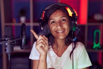 Sticker - Young hispanic woman playing video games wearing headphones smiling happy pointing with hand and finger to the side