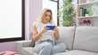 © Krakenimages.com - Young blonde woman watching video on smartphone sitting on sofa with serious face at home