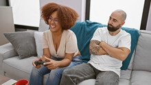 Beautiful interracial couple, looking upset, sit together at home playing video game - love connection tested in living room!
