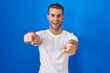 © Krakenimages.com - Young caucasian man standing over blue background pointing to you and the camera with fingers, smiling positive and cheerful