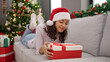 © Krakenimages.com - Young beautiful hispanic woman unpacking gift sitting by christmas tree at home